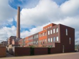 a brick mill with a chimney and clouds in the background